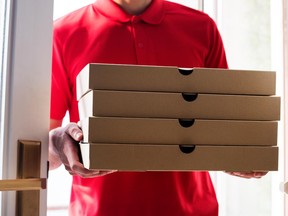 In this stock photo, a pizza delivery man enters a home holding pizzas.