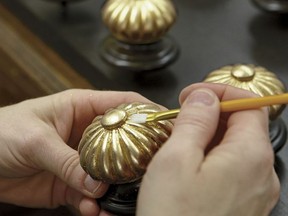 In this photo provided by Ethan Allen, a craftsman uses a small artists brush to press the gold leafing material into the detailed carved elements of the finial on an Ethan Allen Georgetown Bed in their North American workshops. (Ethan Allen via AP)