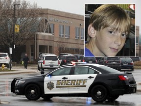 A law enforcement officer walks in front of Great Mills High School, the scene of a shooting, Tuesday, March 20, 2018, in Great Mills alongside a 2014 Facebook profile picture of 17-year-old suspect Austin Rollins.