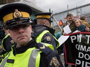 An RCMP officer reads a court order to Federal Green Party Leader Elizabeth May, right, and NDP MP Kennedy Stewart, second right, before they were arrested after joining protesters outside Kinder Morgan's facility in Burnaby, B.C., on Friday March 23, 2018.