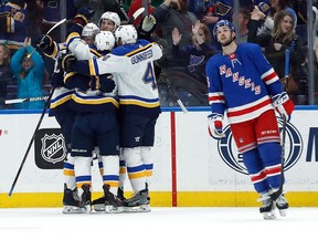 Members of the St. Louis Blues surround teammate Alex Pietrangelo after his goal as New York Rangers' Ryan Sproul, right, skates past during an NHL game on March 17, 2018