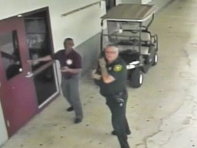 This Feb. 14, 2018 frame from security video provided by the Broward County Sheriff's Office shows deputy Scot Peterson, right, outside Marjory Stoneman Douglas High School in Parkland, Fla.