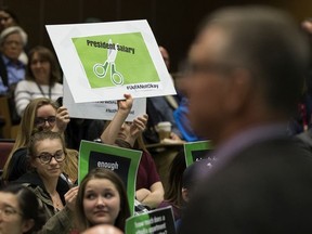 Students hold up protest signs during a campus forum held by University of Alberta president David Turpin (right), in Edmonton on Wednesday March 28, 2018.