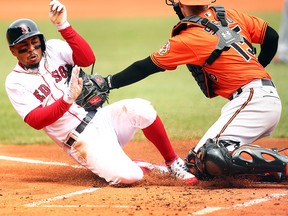 Mookie Betts of the Boston Red Sox slides safely into home plate as the ball gets away from Chance Sisco of the Baltimore Orioles in the first inning of a game at Fenway Park on April 14, 2018 in Boston. (Adam Glanzman/Getty Images)