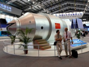 In this Nov. 16, 2010 file photo, visitors sit beside a model of China's Tiangong-1 space station at the 8th China International Aviation and Aerospace Exhibition in Zhuhai in southern China's Guangdong Province.