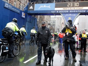 Bicycle-mounted police officers pass a Boston Special Operations K-9 police officer and his dog as they patrol at the finish line before the 122nd Boston Marathon on April 16, 2018