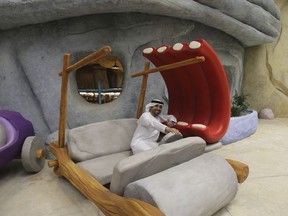 An Emirati poses with Fred Flintstone's mock-up car at the Warner Bros. World amusement park in Abu Dhabi, United Arab Emirates, Wednesday, April 18, 2018. Abu Dhabi will open a $1 billion indoor Warner Bros. amusement park this July, officials announced Wednesday, the latest offering in a crowded market in the United Arab Emirates where one marquee park already faces serious financial problems.