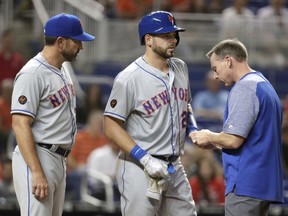 New York Mets catcher Kevin Plawecki, centre, has his hand looked at after being hit by a pitch Wednesday, April 11, 2018, in Miami.