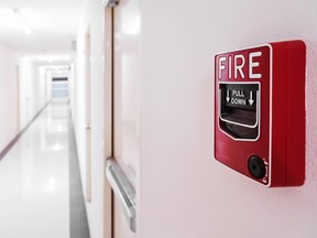 In this stock photo, a fire alarm sits near an exit door in an empty hallway.