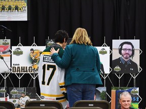 Mourners comfort each other as they look at photographs prior to a vigil at the Elgar Petersen Arena, home of the Humboldt Broncos, to honour the victims of a fatal bus accident in Humboldt, Sask. on Sunday, April 8, 2018. THE CANADIAN PRESS/Jonathan Hayward