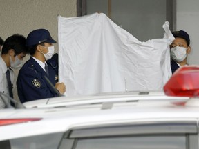 Police officers hide the face of arrested Japanese Yoshitane Yamasaki with a sheet while escorting him to a police vehicle to leave for Prosecutor's Office for further investigation, in Sanda City, western Japan, Monday, April 9, 2018.