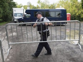 An RCMP officer moves a barricade as they wait for the arrival of asylum seekers crossing the border into Canada from the United States at a police checkpoint close to the Canada-U.S. border near Hemmingford, Que., on Aug. 3, 2017.