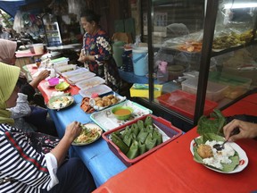 Customers eat nasi uduk, which is Indonesian style steamed rice cooked in coconut milk dish, at street food stall in Jakarta, Indonesia. Tuesday, April 3, 2018. Judges on a popular British cooking show are being ridiculed for ignorance of Asian food after insisting the chicken in a Malaysian contestant's rendang curry should have been crispy.