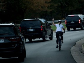 This file photo taken on October 28, 2017 shows a woman on a bike gestures with her middle finger as a motorcade with US President Donald Trump departs Trump National Golf Course in Sterling, Virginia.