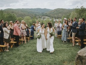In this May 28, 2017 photo provided by Jamie Mercurio, Lib Tietjen, right, and her wife, Claire Skrivanos, walk up the aisle after their wedding ceremony in Fairlee, Vt. Traditional weddings are deeply rooted in gender-based rituals. But the growing LGBTQ wedding industry is coming up with new approaches. Many couples are engaging with centuries of tradition but crafting their own way to the altar.
