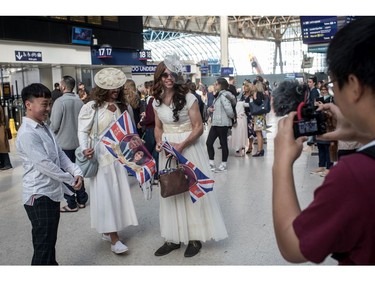 LONDON, ENGLAND - MAY 19: People take photographs with two men wearing wedding dresses while waiting for a train to Windsor to watch the Royal Wedding of Prince Harry and Meghan Markle at Waterloo train station on May 19, 2018 in London, England. The marriage of Britain's Prince Harry and US actress Meghan Markle is being held in Windsor today at the St George's Chapel in Windsor Castle.
