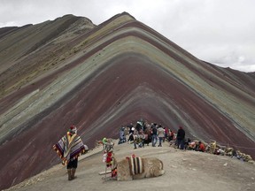 In this March 2, 2018 photo, an Andean man rests with his llama on Rainbow Mountain in Pitumarca, Peru. Tourists gasp for breath as they climb for two hours to the 16,404-foot (5,000-meter) peak in the Peruvian Andes, but stunned by the magical beauty that unfurls before them.