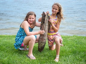 In this Wednesday, May 30, 2018 photo, Paige Burnett, 10, left, and Sage Menzies, 9,  pose with a First World War practice bomb they discovered the day before while swimming in Lobdell Lake behind the Menzies' home in Linden, Mich.