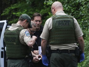 In this Saturday, May 19, 2018 file photo, Washington State Fish and Wildlife Police confer with an individual from the King County Medical Examiner's and a King County Sheriff's deputy on a remote gravel road above Snoqualmie,  following a fatal cougar attack.