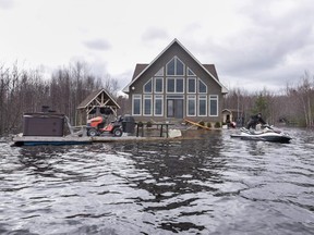Mike Roy uses a personal watercraft to pull a dock loaded with a hot tub and lawnmower as floodwaters surround his home on Grand Lake, N.B. on Tuesday, May 1, 2018.