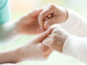 In this stock photo, a young woman holds hands with an elderly woman.