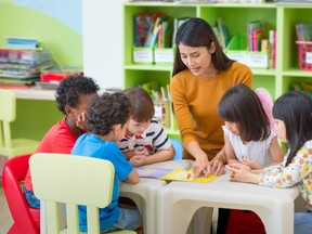 Asian female teacher teaching mixed race kids reading book in classroom,Kindergarten pre school concept.