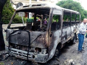 In this photo released by the Syrian official news agency SANA, Syrians gather next to a burnt bus hit in shelling, apparently by Islamic State fighters, in Damascus, Syria, Wednesday, May 9, 2018. Militants fired three mortar shells on the center of Damascus Wednesday killing several persons and wounding 14, Syria's state news agency said. (SANA via AP)