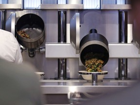 Customers wait as their automatically prepared food is dropped from a cooking pot into a bowl at Spyce, a restaurant which uses a robotic cooking process in Boston, Thursday, May 3, 2018.
