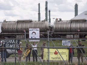 Protestors stand outside the fence as Prime Minister Justin Trudeau visits Kinder Morgan in Edmonton Alta, on Tuesday June 5, 2018. A study by a sustainable energy research group predicts the federal government's purchase of the Trans Mountain pipeline will add significantly to the deficit next year.