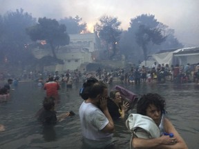 In this Monday, July 23, 2018 image from video provided by Elia Kallia, people escaping wildfires wade into the waters of the "Silver Coast" beach in Mati, Greece. (Elia Kallia via AP)