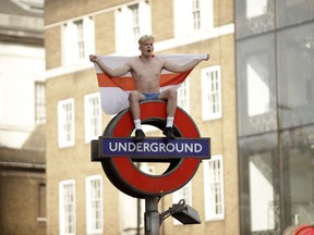 An England soccer fan sits with a St George's Cross England flag atop of a London Underground subway sign in the London Bridge area after England won their quarterfinal match against Sweden, at the 2018 soccer World Cup, Saturday, July 7, 2018.