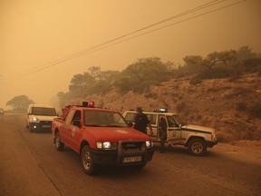 Smoke fills the sky as members of the emergency services block a road near Kineta, west of Athens, Monday, July 23, 2018.