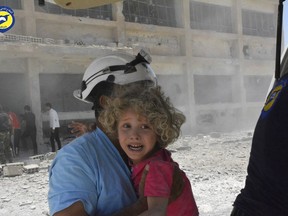 In this June 14, 2017, file photo, provided by the Syrian Civil Defence group known as the White Helmets, shows a civil defence worker carrying a child after airstrikes hit a school housing a number of displaced people in the western part of the southern Daraa province of Syria.