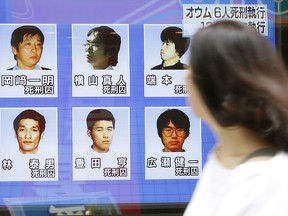 A woman walks on a street while watching TV news reporting executions of six members of Aum Shinrikyo, in Tokyo Thursday, July 26, 2018. (Shinji Kita/Kyodo News via AP)