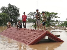 Villagers take refuge on a rooftop above flood waters from a collapsed dam in the Attapeu district of southeastern Laos, Tuesday, July 24, 2018. The official Lao news agency KPL reported Tuesday that the Xepian-Xe Nam Noy hydropower dam in Attapeu province collapsed Monday evening, releasing large amounts of water that swept away houses and made more than 6,600 people homeless. (Attapeu Today via AP) ORG XMIT: BKWS303