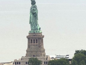 In this image taken from video, people climb on the pedestal of the Statue of Liberty in New York Harbor Wednesday, July 4, 2018. A person scaled the statue's base and forced its evacuation shortly after several other people were arrested for hanging a banner from the pedestal that called for abolishing the Immigration and Customs Enforcement agency. (AP Photo)