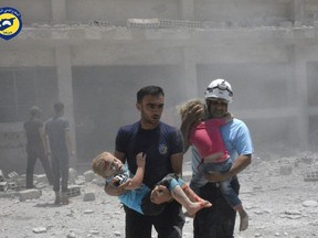 FILE - In this Wednesday, June 14, 2017, file photo, provided by the Syrian Civil Defense group known as the White Helmets, shows civil defense workers carrying children after airstrikes hit a school housing a number of displaced people, in the western part of the southern Daraa province of Syria. The Israeli military said Sunday it had rescued members of a Syrian volunteer civil organization, known as White Helmets, from the volatile frontier area and evacuated them to a third country, the first such Israeli intervention in Syria's lengthy civil war.