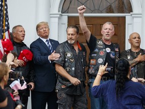 U.S. President Donald Trump stands in the rain with members of Bikers for Trump and supporters after saying the Pledge of Allegiance, Saturday, Aug. 11, 2018, at the clubhouse of Trump National Golf Club in Bedminster, N.J.