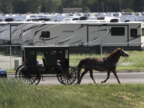 An Amish family rides their horse and buggy past a storage lot for recreational vehicles in Goshen, Ind., on Friday, June 1, 2018. (AP Photo/Charles Rex Arbogast)