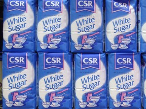 Bags of white sugar are stacked on the shelves in a supermarket.