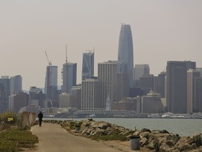 A man rides a scooter on Treasure Island as the San Francisco city skyline sits in a smoky haze in the background Wednesday, Aug. 8, 2018.