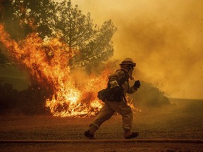 A firefighter runs while trying to save a home as a wildfire tears through Lakeport, Calif., Tuesday, July 31, 2018. The residence eventually burned.