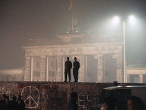 FILE - In this Nov. 14, 1989 file photo two East German border guards patrolled atop of Berlin Wall with the illuminated Brandenburg Gate in background, in Berlin. An artist collective plan to rebuild the Berlin wall during an art project in Berlin in October.