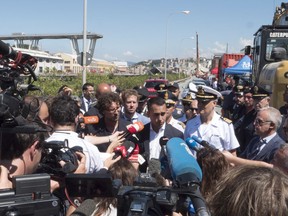 Italian Deputy Premier Luigi Di Maio, centre right, and Italian Transport and Infrastructure Minister Danilo Toninelli, centre left with glasses, speak to the media in front of the collapsed Morandi highway bridge in Genoa, northern Italy, Wednesday, Aug. 15, 2018.