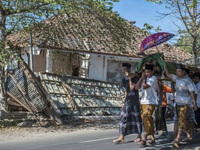 Indonesian men carry the body of a victim of last week's earthquake past a damaged building during a funeral in Gangga, Lombok Island, Indonesia, Sunday, Aug. 12, 2018.