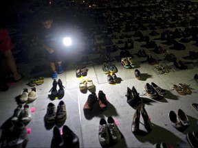 In this June 1, 2018 file photo, a child shines a light on hundreds of shoes at a memorial for those killed by Hurricane Maria, in front of the Puerto Rico Capitol in San Juan. /, File) ORG XMIT: XLAT115
