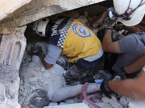 Syrian White Helmet civil defence workers remove a body from the rubble at the scene of an explosion that brought down a five-story building, in the village of Sarmada, Syria, Sunday, Aug. 12, 2018. (Syrian Civil Defense White Helmets via AP)