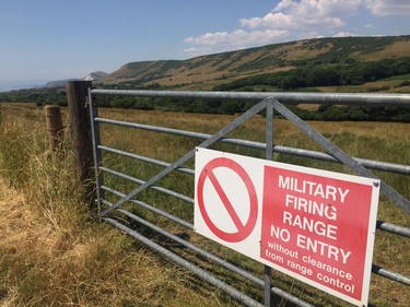 In this July 8, 2018 photo, a British Ministry of Defense sign warns visitors that they are on a firing range near Dorset, England. The adjacent road leads to Tyneham, a village which was ordered evacuated in 1943 to provide extra land for military exercises, ahead of D-Day. The people have never been allowed back and the village remains in the hands of the military and has become a tourist attraction, providing a poignant and unusual reminder of World War II.