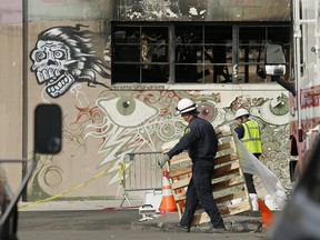 A member of the Alameda County Sheriff's Department, left, carries away a pallet outside the site of a warehouse fire in Oakland, Calif. on Wednesday, Dec. 7, 2016.