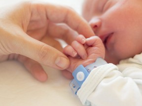 In this stock photo, a newborn baby boy sleeps in his crib while his mother holds his hand.